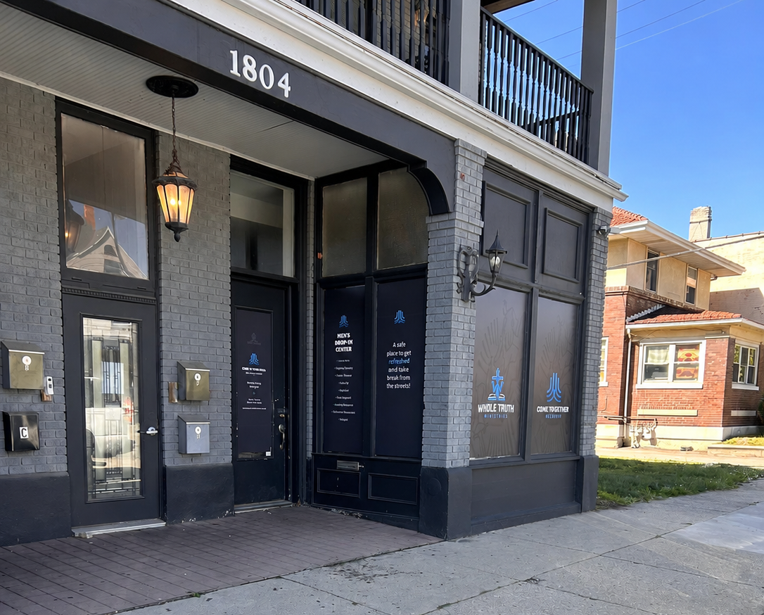Exterior sidewalk view of The Well men’s drop-in center in Dayton, Ohio, showing the storefront and window signage.