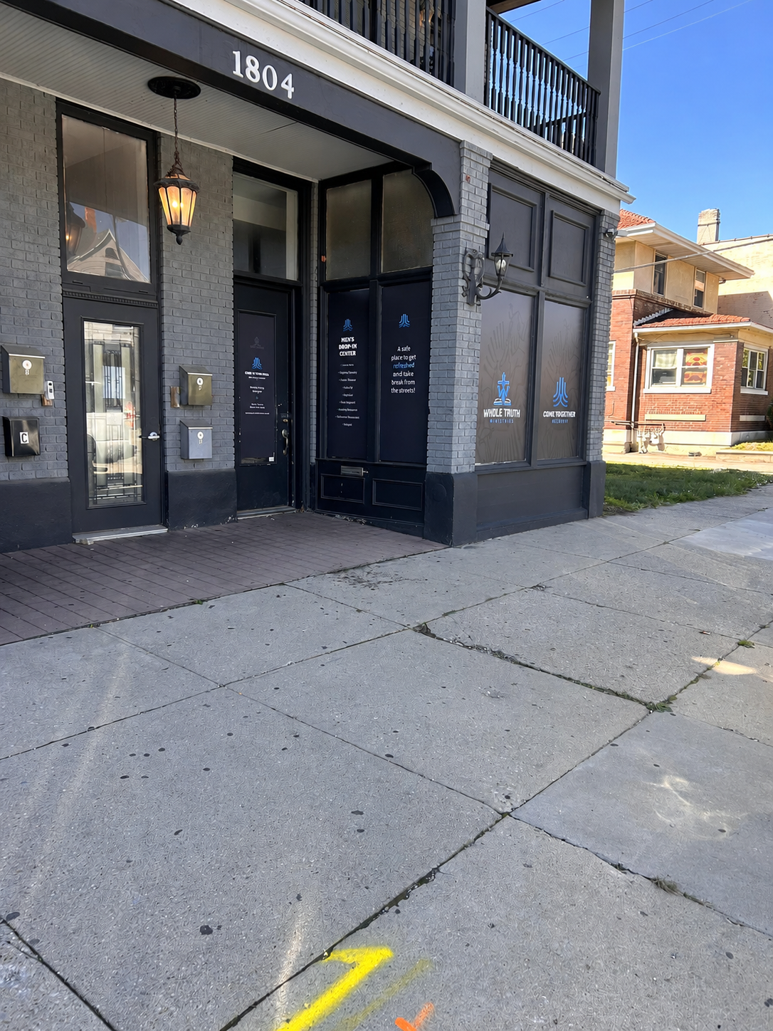 Exterior sidewalk view of The Well men’s drop-in center in Dayton, Ohio, showing the storefront and window signage.